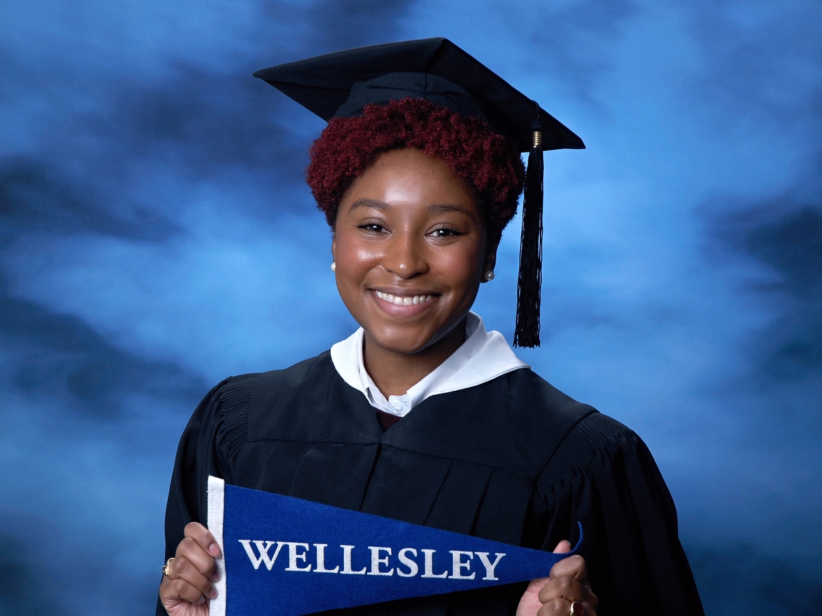 Samuels in cap and gown holding a commemorative Wellesley College flag