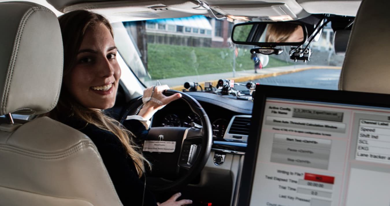 Young woman driving looking back with a computer monitoring the drive